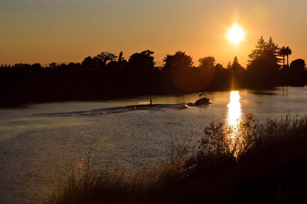 Recreational boaters on the water with someone water-skiing behind the boat in the Sacramento-San Joaquin Delta during sunset. Photo by ZoArt Photography.