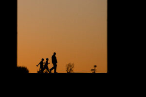 The silhouettes of an adult and two children walking in the Delta after sunset.