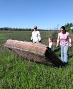 Two adult women and a young girl wearing gloves, moving a large old and damaged mattress in the grass at the Waterway Cleanup.