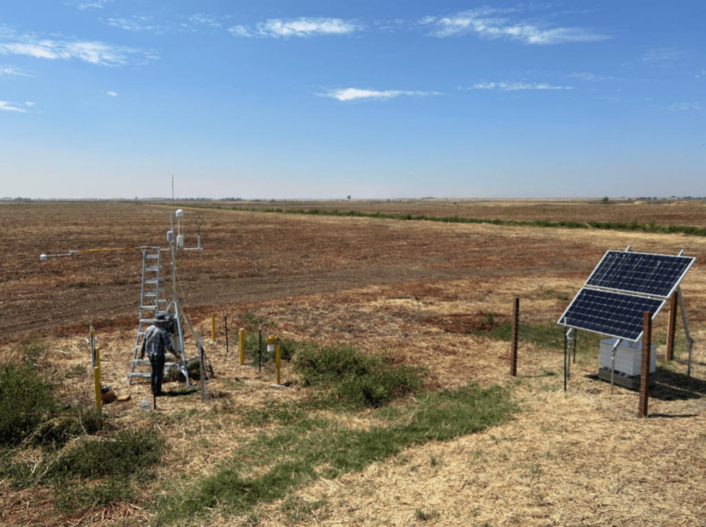 An eddy covariance tower in a field. A person stands in the foreground near a ladder.